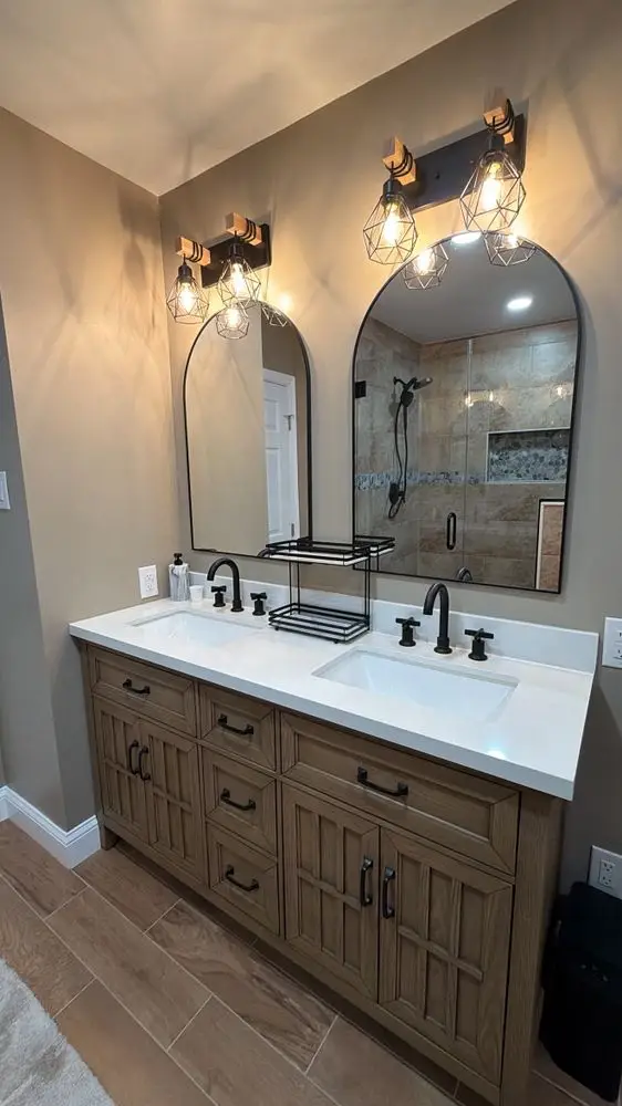 Bathroom with a double white oak vanity, arched black-framed mirrors, black faucets and industrial-style sconces — a completed CMD Property Restoration Group project