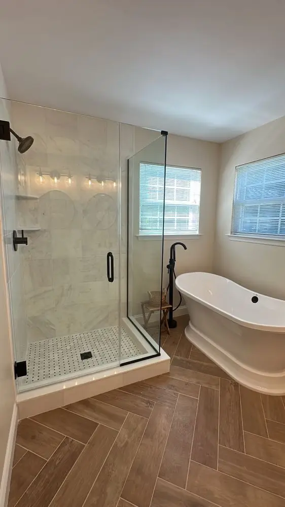 Bathroom with a freestanding soaking tub, frameless glass shower with black hardware and wood-look tile floor — a completed CMD Property Restoration Group project