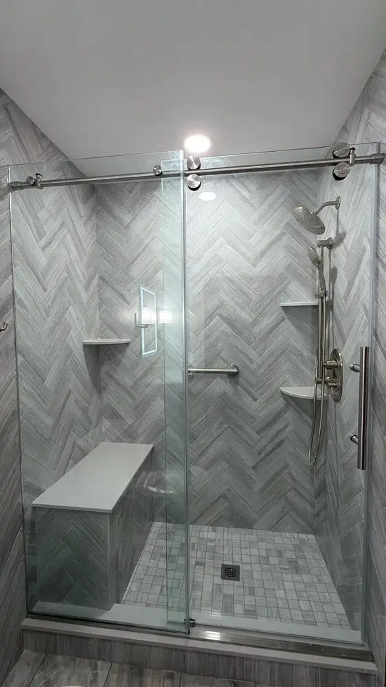 Walk-in shower with gray herringbone tile, a built-in bench, corner niche and sliding frameless glass door — a completed CMD Property Restoration Group project