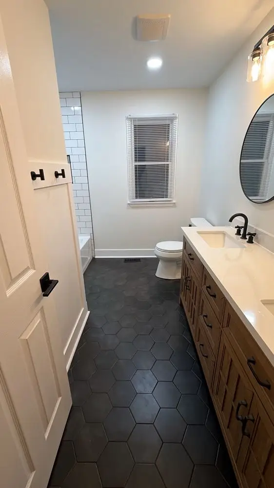 Bathroom with dark hexagon floor tile, a white oak vanity, round mirror and matte black fixtures — a completed CMD Property Restoration Group project
