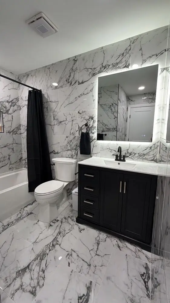 Bathroom with bookmatched marble-look wall tile, a black vanity, backlit mirror and chrome fixtures — a completed CMD Property Restoration Group project