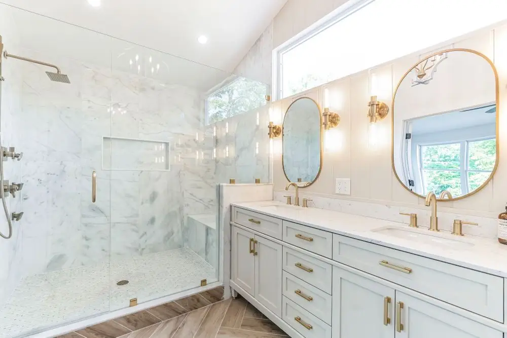CMD bathroom with a marble-look shower, brass fixtures and a white double vanity