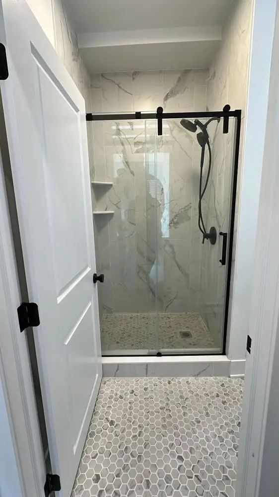 Walk-in shower with marble-look wall tile, a black sliding glass door and patterned mosaic floor — a completed CMD Property Restoration Group project