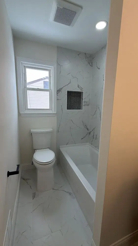 Tub-shower with marble-look tile, a recessed niche and brass fixtures — a completed CMD Property Restoration Group project