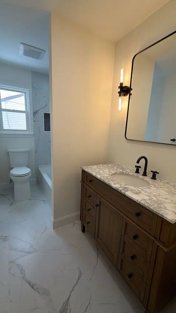Bathroom with a white oak vanity, marble countertop and floor, black-framed mirror and black faucet — a completed CMD Property Restoration Group project