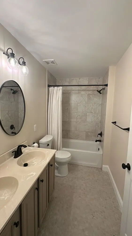 Full bathroom with a tiled tub-shower, gray vanity, oval mirror and black fixtures — a completed CMD Property Restoration Group project