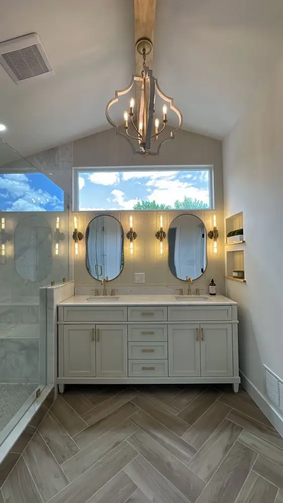 Vaulted bathroom with a white double vanity, oval mirrors, a chandelier, transom window and herringbone floor — a completed CMD Property Restoration Group project