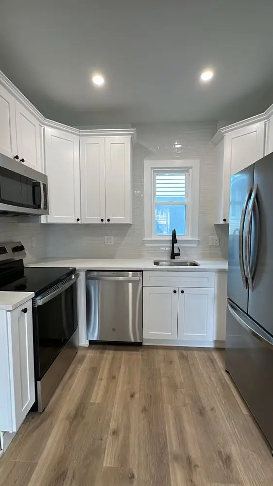 Compact kitchen with white shaker cabinets, black hardware, stainless appliances and light oak flooring — a completed CMD Property Restoration Group project