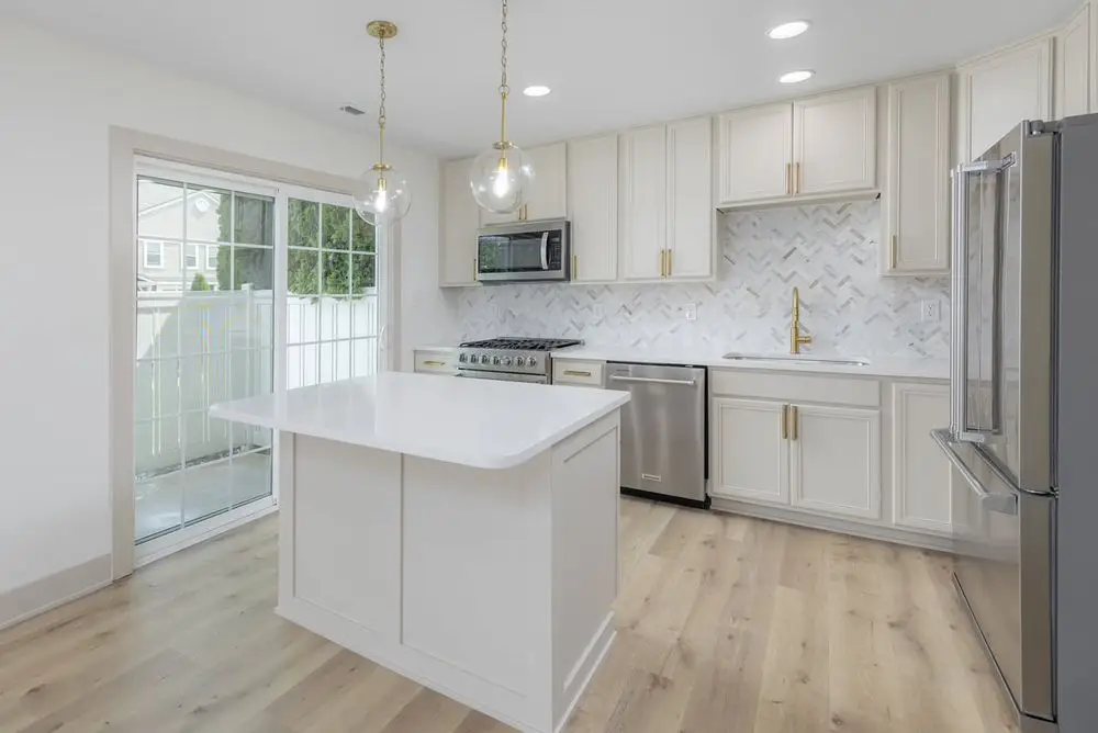 White kitchen with a quartz island, herringbone tile backsplash, brass pendants and stainless appliances — a completed CMD Property Restoration Group project