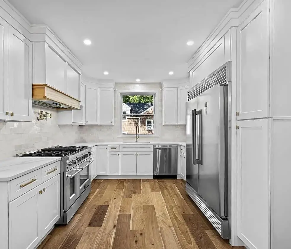 Farmhouse kitchen with full-height white cabinetry, a professional-style range and wood-trimmed hood, brass hardware and walnut-tone floors — a completed CMD whole-home renovation