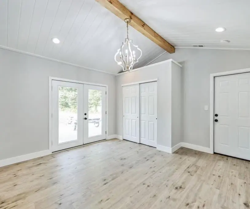 Bedroom with a vaulted shiplap ceiling, exposed beam, chandelier and French doors — a completed CMD whole-home renovation