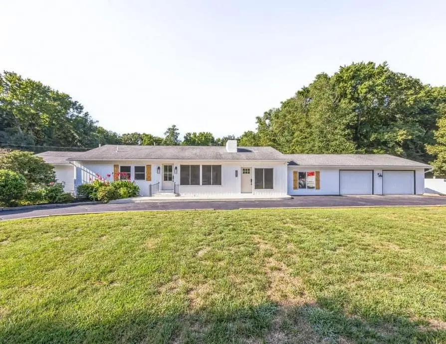 Exterior of a single-story ranch after renovation — white siding, new front entry and garage doors, lawn and driveway — a completed CMD whole-home renovation