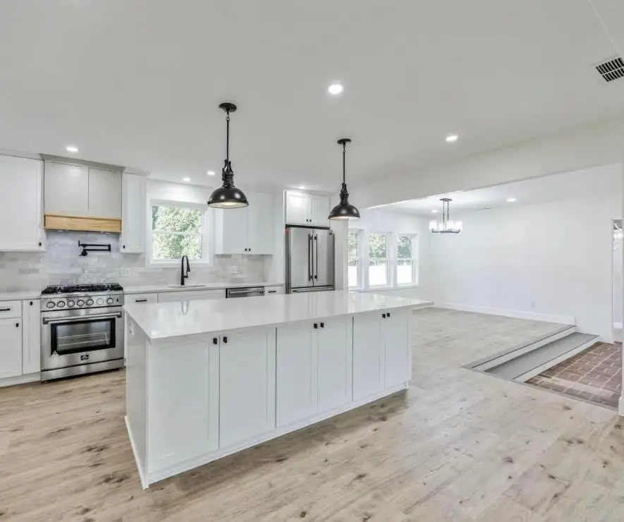 Renovated ranch kitchen open to the living area with a white shaker island, professional range, black pendants and light oak floors — a completed CMD whole-home renovation