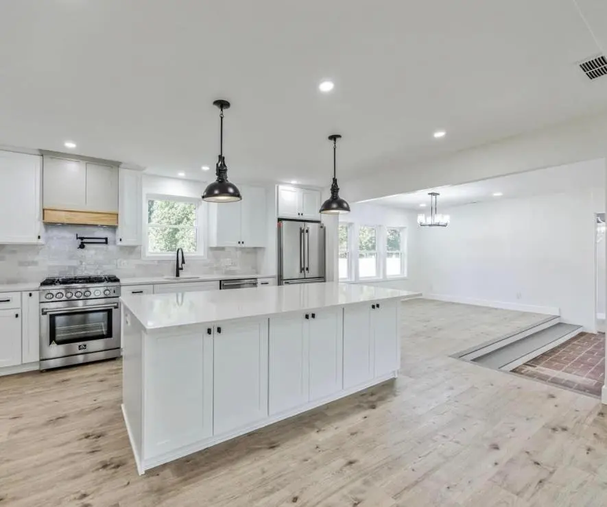 Open ranch kitchen with a white shaker island, professional range, black pendants and continuous light oak floors — a completed CMD whole-home renovation