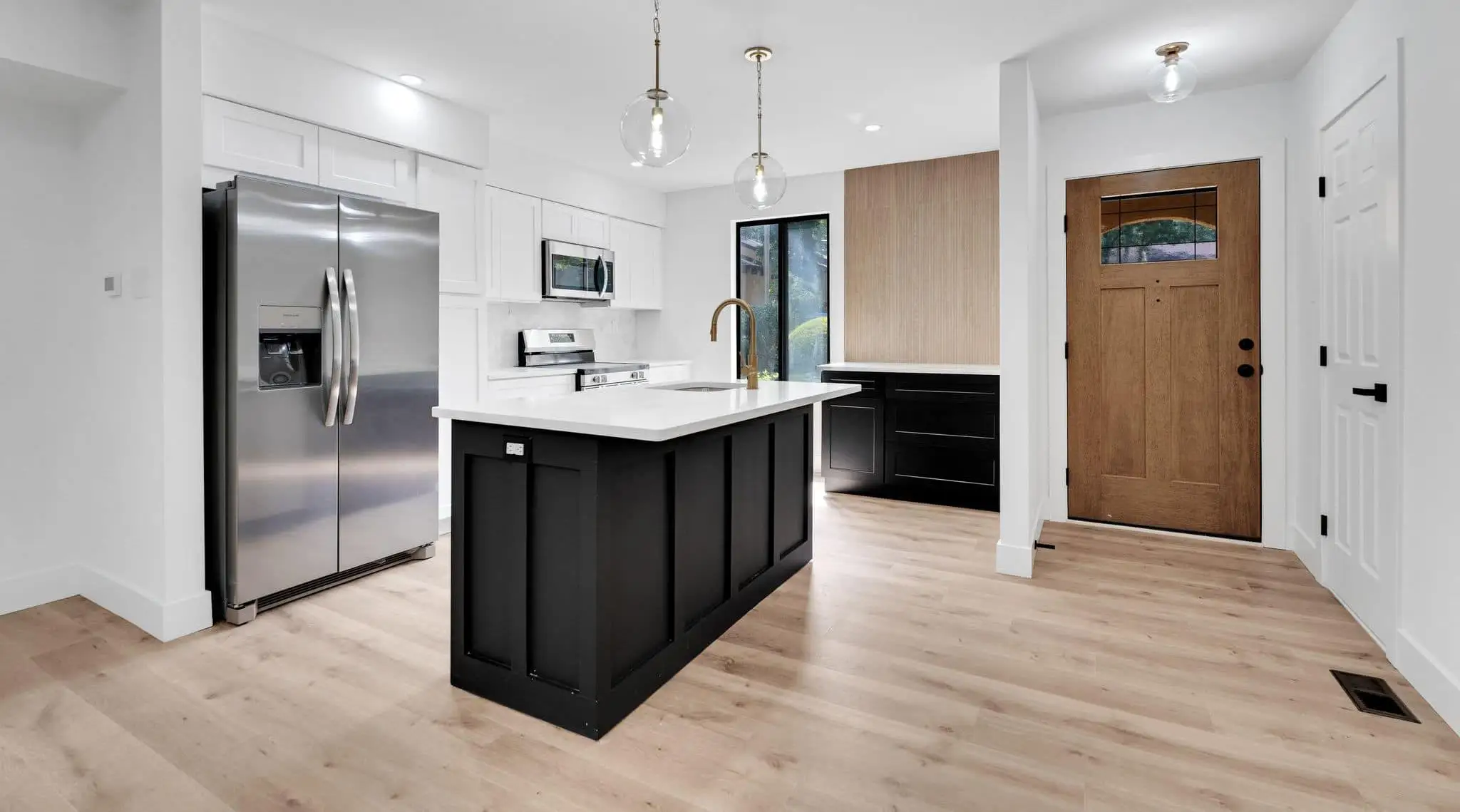 Townhome kitchen with a black shaker island, white cabinetry, wood-slat accent panel and a new wood front door — a completed CMD whole-home renovation