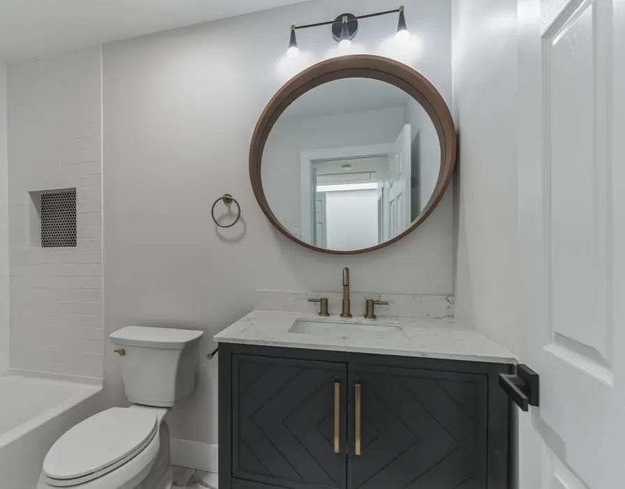 Powder room with a black vanity, marble top, brass fixtures and a round wood-framed mirror — a completed CMD whole-home renovation